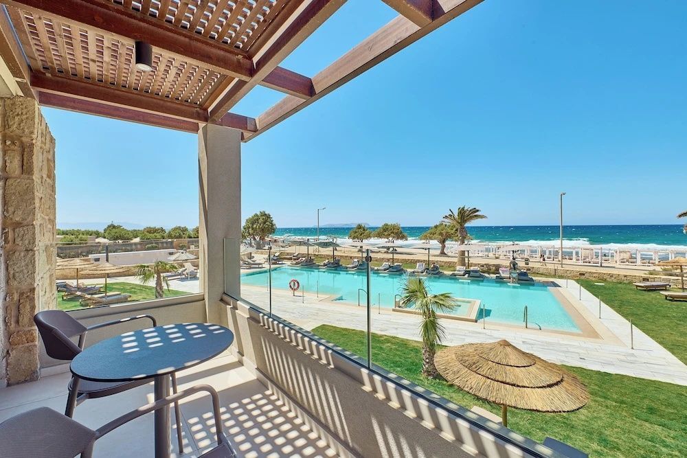 Aussicht von der überdachten Terrasse auf den Außenpool, Palmen und den dahinterliegenden Strand.
