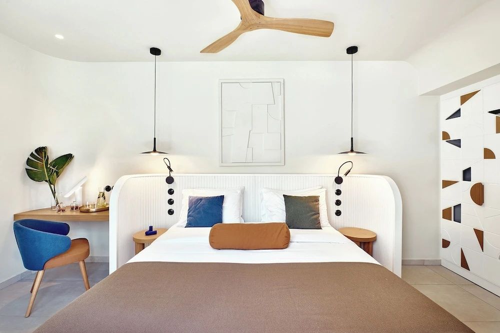 Doppelbett mit weißem Kopfteil, brauner Tagesdecke und einem Deckenventilator aus Holz.