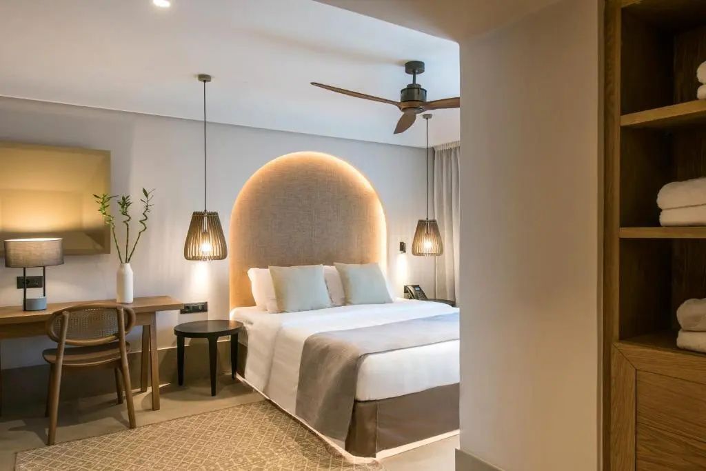 Doppelbett mit beleuchtetem rundem Kopfteil und Hängeleuchten im Hotelzimmer.