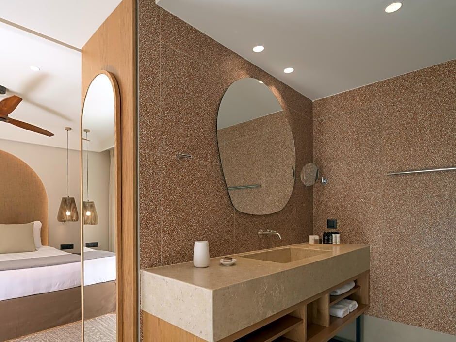 Badezimmer mit modernem Steinwaschtisch, organischem Spiegel und Fliesen.