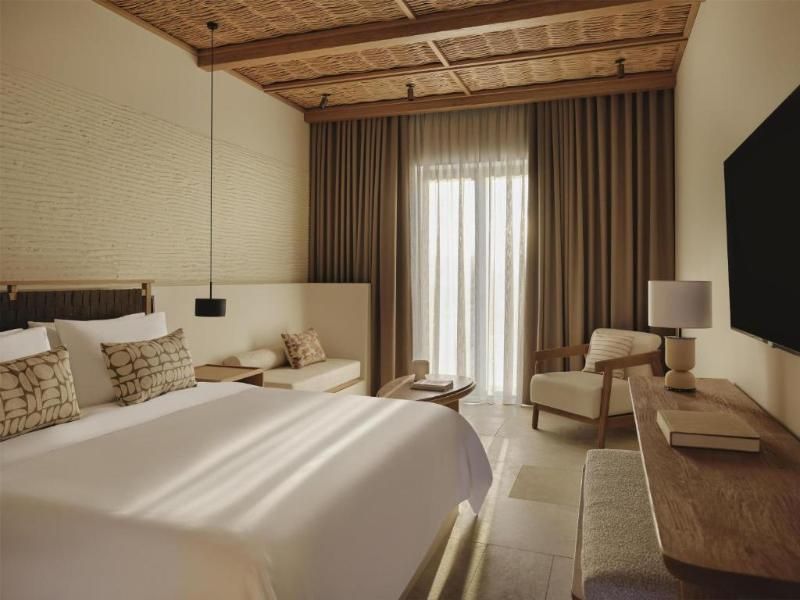 Helles Hotelzimmer mit Doppelbett, gemütlichem Sitzbereich und Holzdecke.