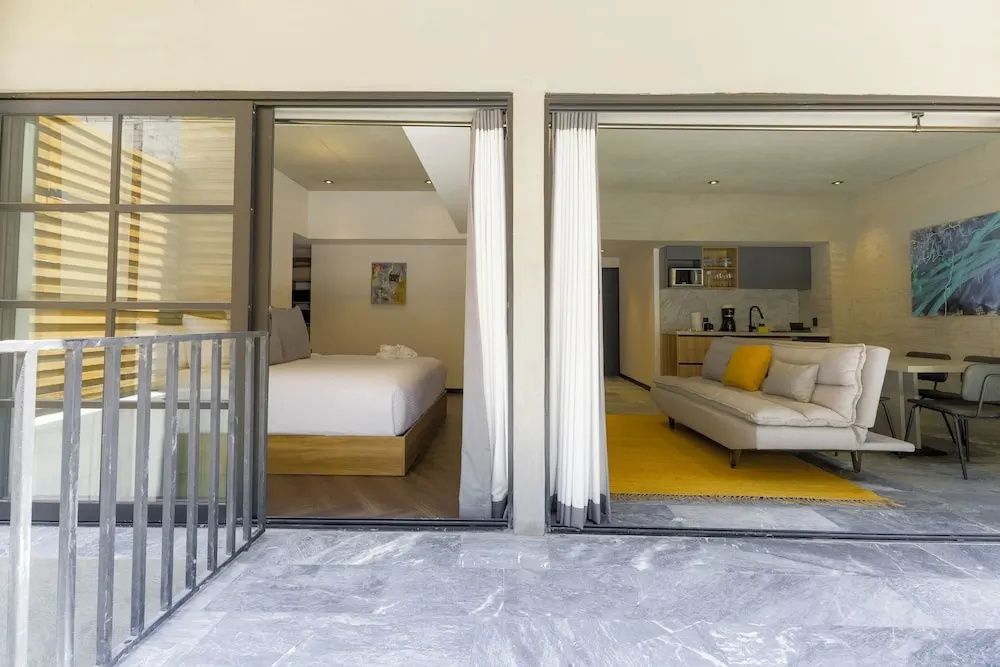 Blick durch geöffnete Schiebetüren in ein Apartment mit Doppelbett, Sofa und einer Küchenzeile.