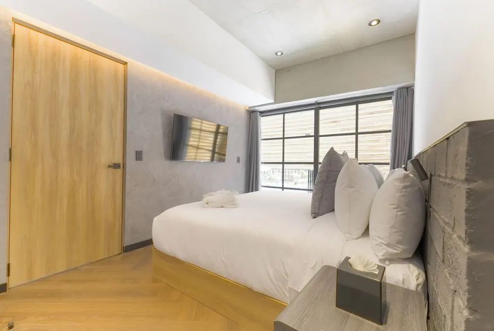 Modernes Schlafzimmer mit Doppelbett, Fernseher an der Wand und großer Fensterfront.