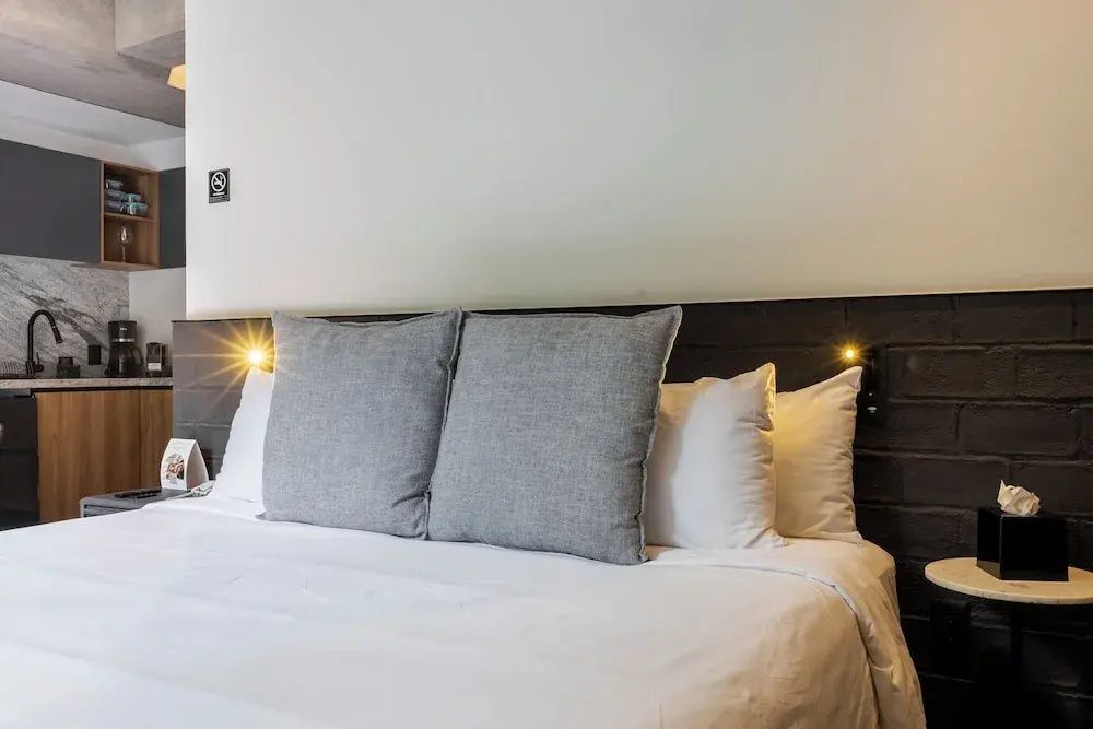 Doppelbett mit weisser Bettwaesche, zwei grauen Dekokissen und integrierter Beleuchtung.