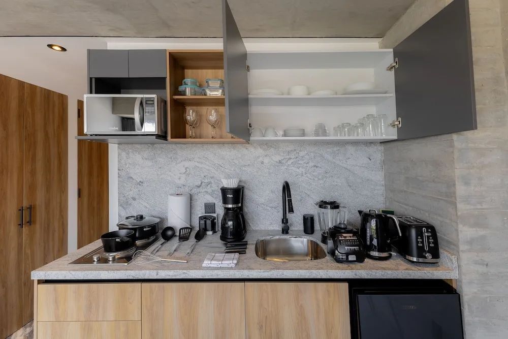Moderne Küchenzeile mit Mikrowelle, Kaffeemaschine, Spüle und Gläsern in Oberschränken.