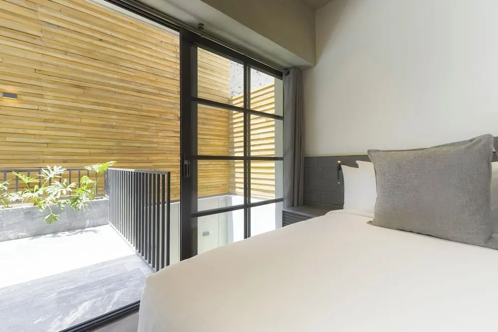 Helles Schlafzimmer mit weiß bezogenem Bett und großer Fensterfront zur Holzverkleidung draußen.