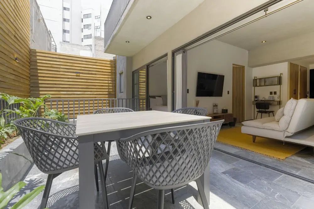 Terrassentisch mit Stühlen vor der geöffneten Schiebetür eines modernen Apartments.