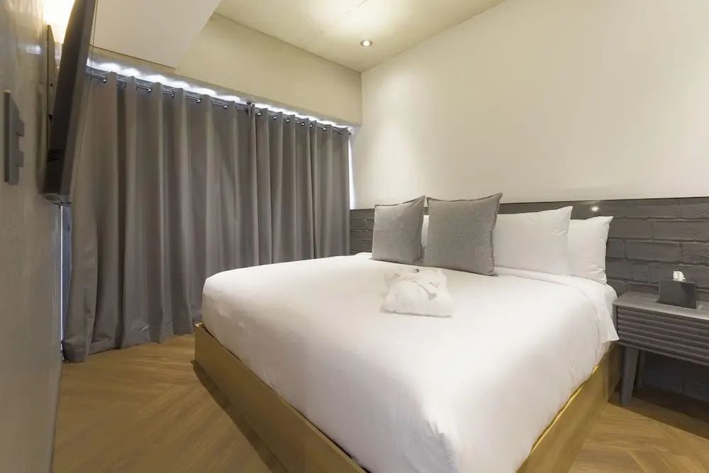Schlafzimmer mit großem Doppelbett, Holzfußboden und zugezogenen grauen Vorhängen.
