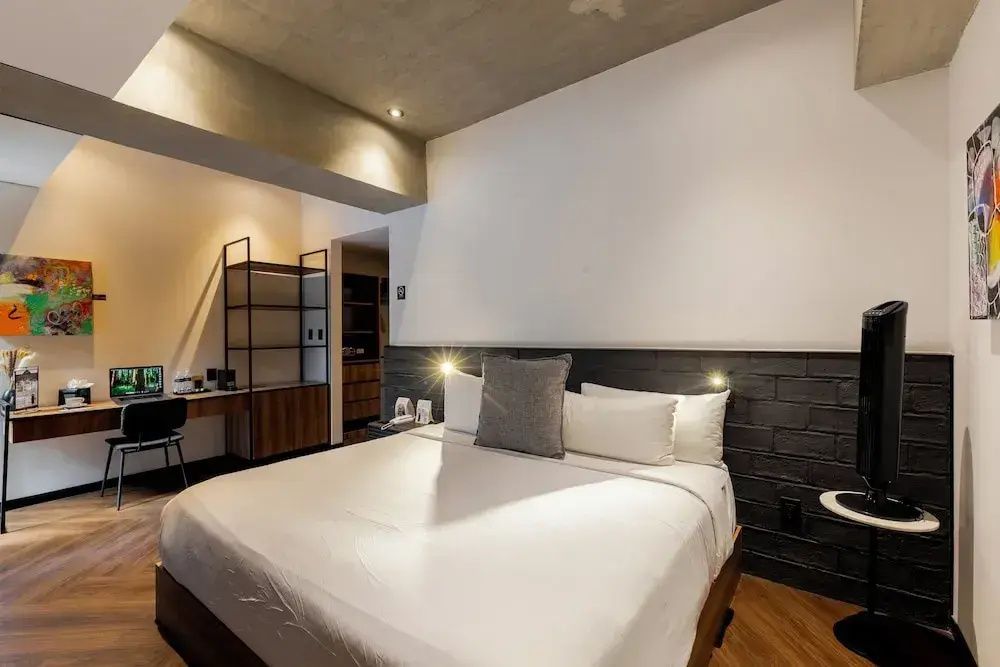 Doppelbett mit weißer Bettwäsche und dunkler Kopfteilwand aus Backstein im Hotelzimmer.