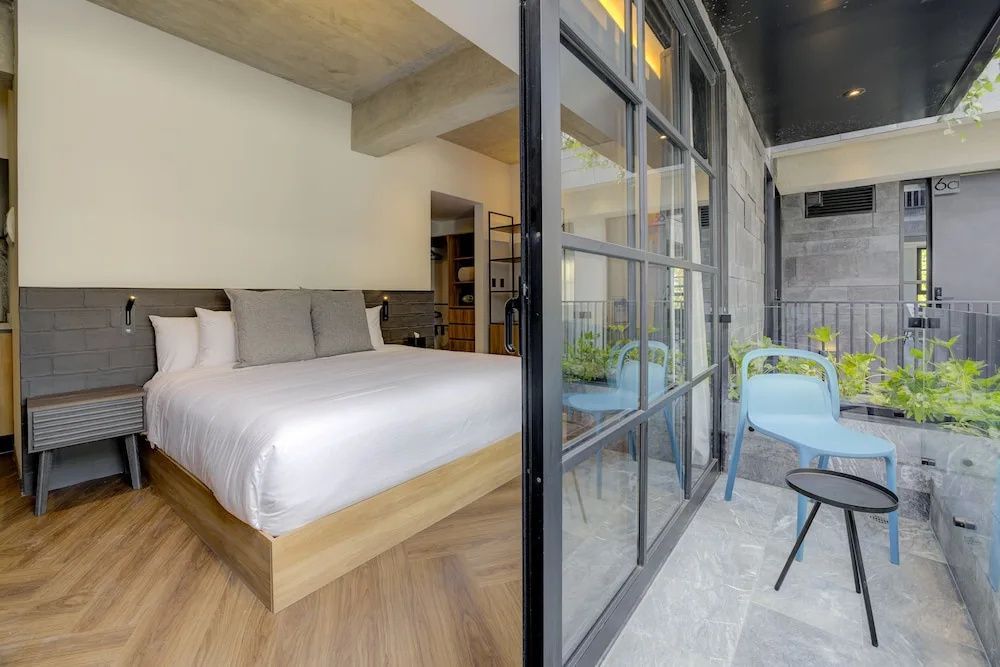 Helles Schlafzimmer mit grossem Bett und Glasfront zum Balkon mit blauen Stuehlen.