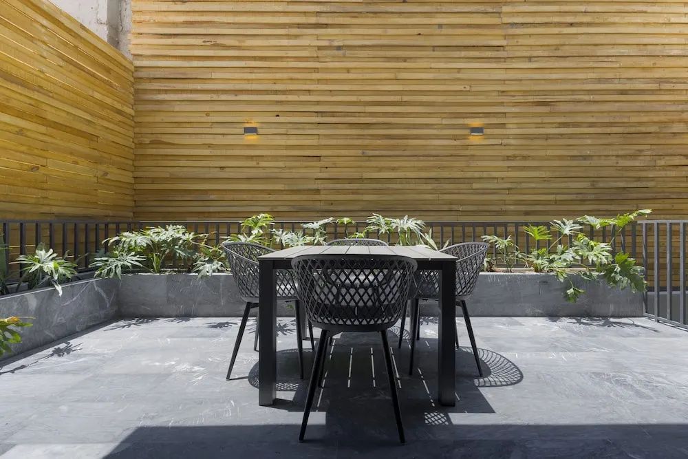 Sitzgruppe auf der Terrasse mit Holzwand und grünen Pflanzen im Hintergrund.