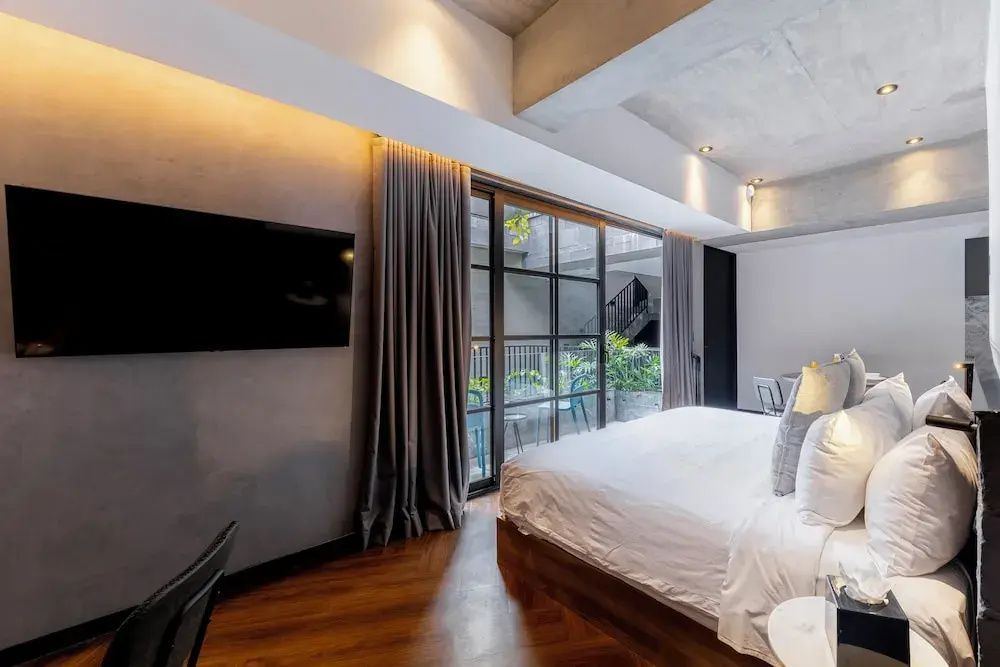 Modernes Doppelzimmer mit Parkettboden, Bett, Wandfernseher und Verglasung.