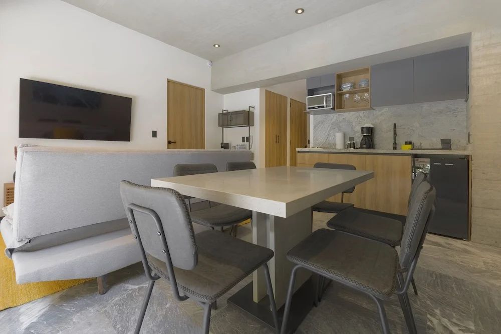 Modernes Esszimmer mit grauem Tisch, Stühlen und einer integrierten Küchenzeile im Hintergrund.