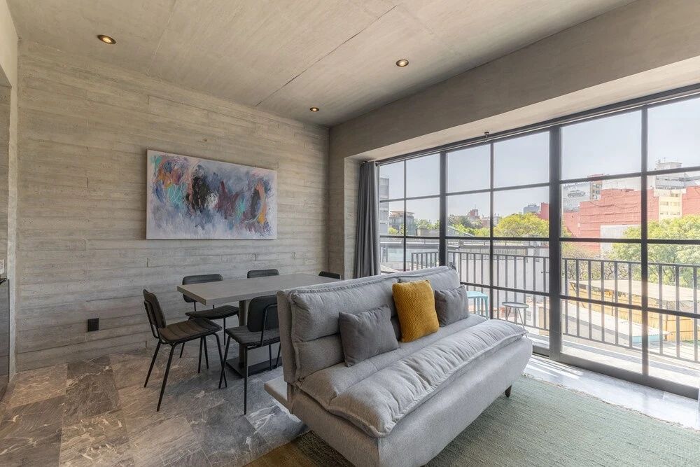 Modernes Wohnzimmer mit grauem Sofa, Esstisch und großen Fensterfronten.