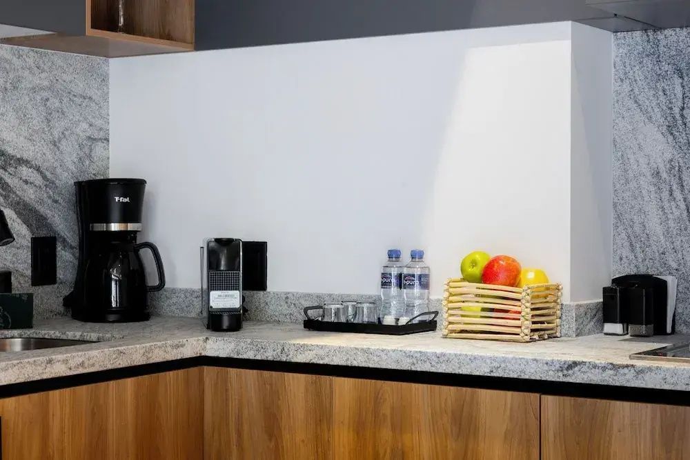 Kuechenzeile aus Holz mit Kaffeemaschine, Wasserflaschen und Obst auf der Arbeitsplatte.
