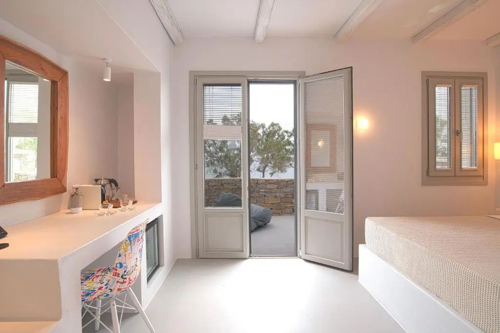 Helles Hotelzimmer mit buntem Stuhl am Schreibtisch und offenem Zugang zur Terrasse.