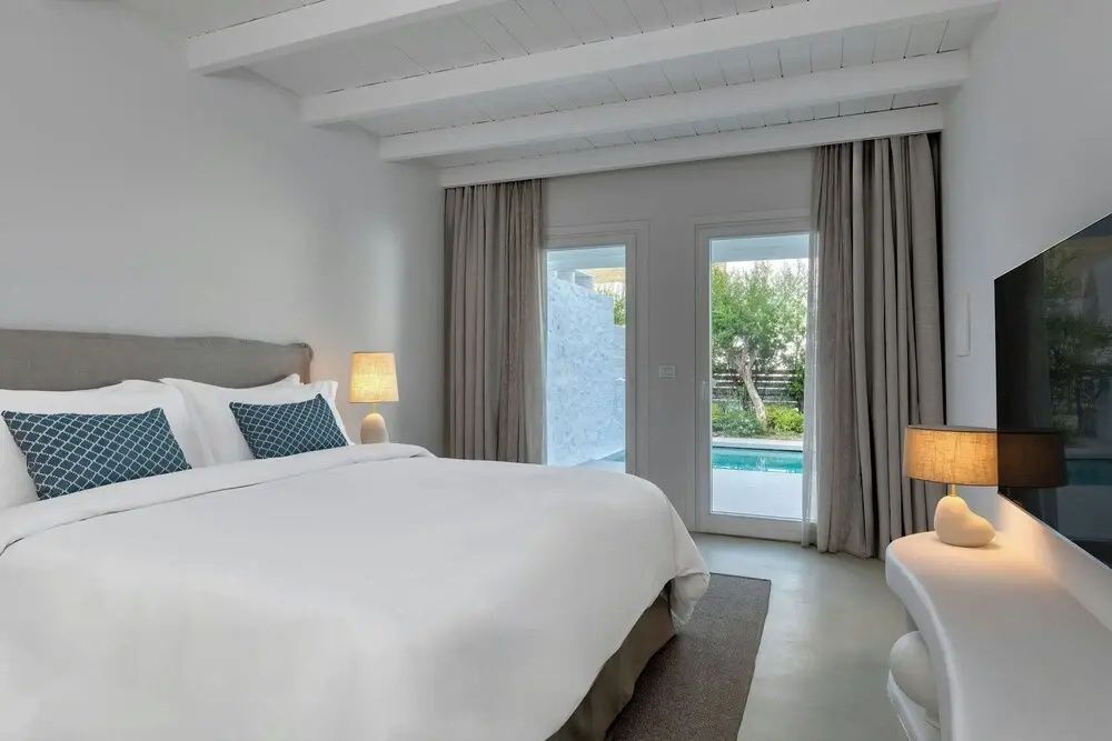 Schlafzimmer mit weißer Bettwäsche, Holzbalkendecke und Zugang zur Terrasse mit Pool.