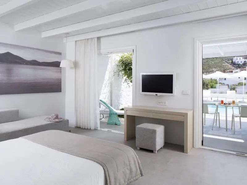 Modernes Hotelzimmer in Weißtönen mit Flachbildfernseher, Schreibtisch und Zugang zur Terrasse.