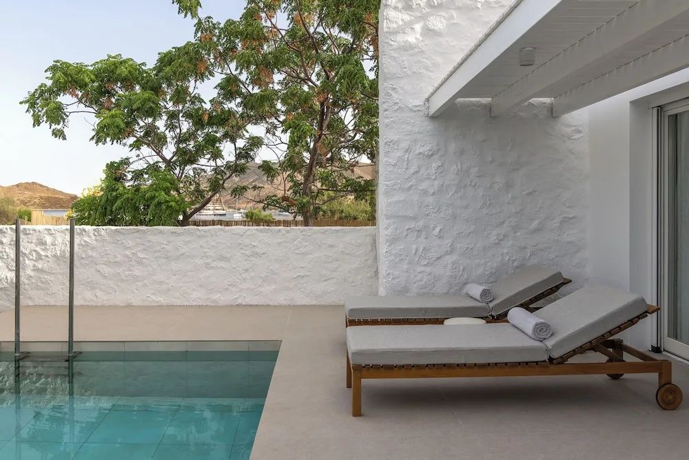 Terrasse mit zwei Sonnenliegen und privatem Pool vor weiß gekalkter Wand.