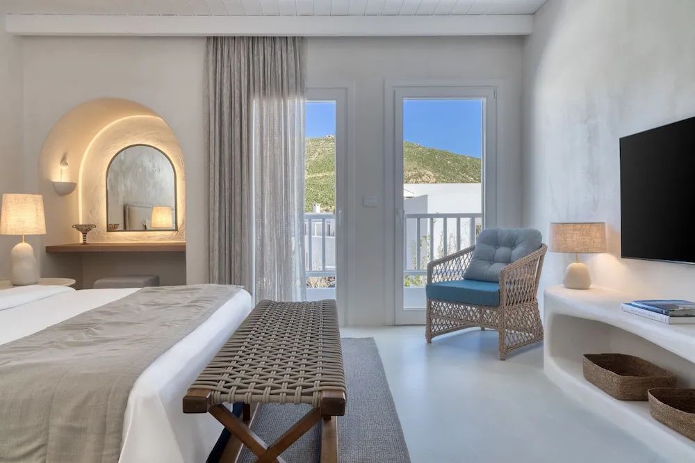 Schlafzimmer mit weißer Einrichtung, Korbsessel und Blick durch die Balkontür.