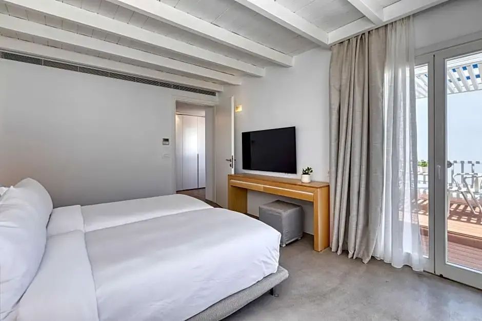 Helles Hotelzimmer mit Doppelbett, Flachbildfernseher auf Holztisch und Balkendecke.