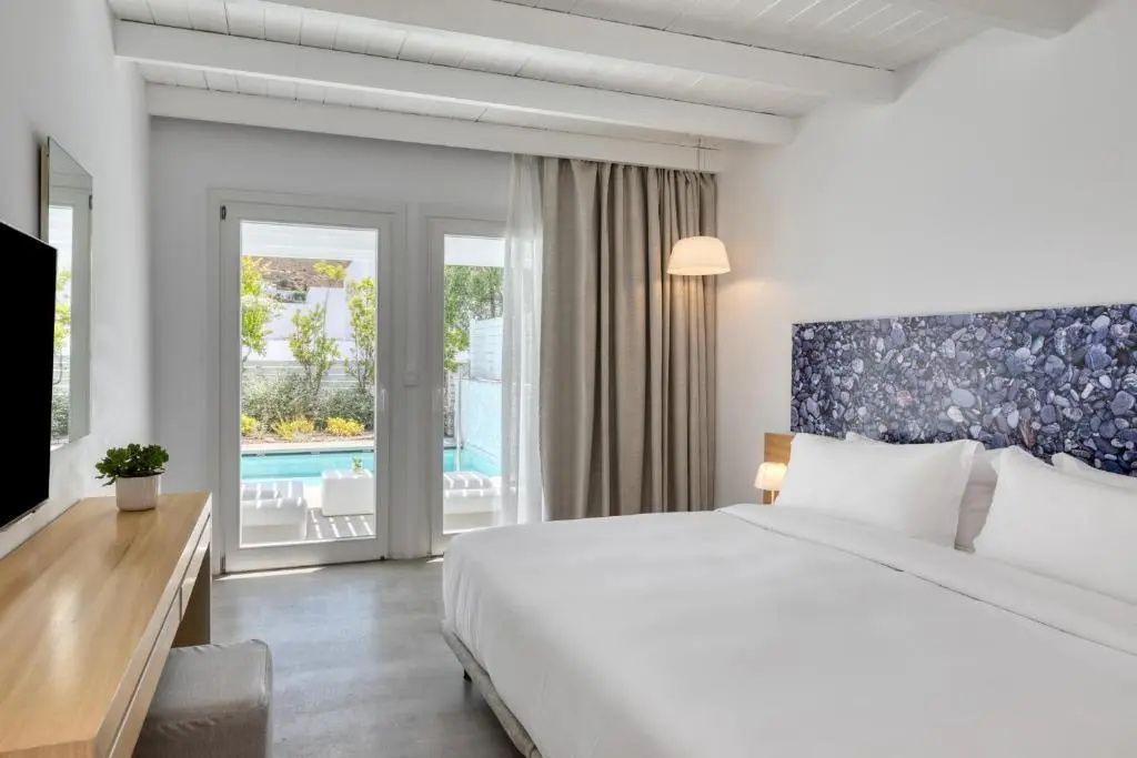 Hell eingerichtetes Schlafzimmer mit Doppelbett und Zugang zu einer Terrasse mit Privatpool.