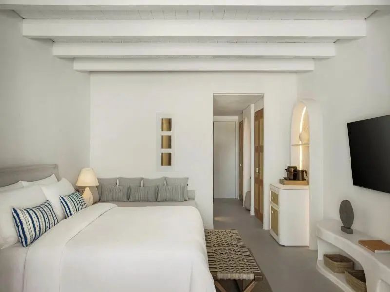 Weiß gestaltetes Schlafzimmer mit Doppelbett, Tagesbett und weißer Holzbalkendecke.
