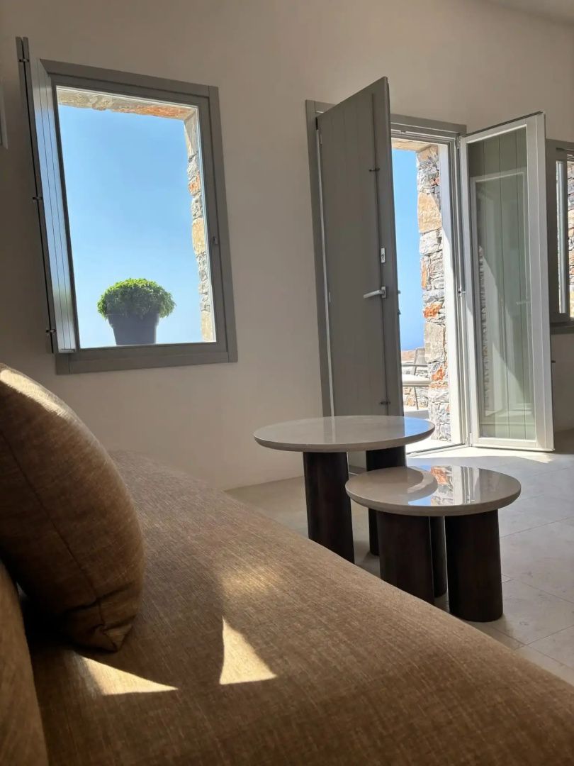 Helles Hotelzimmer mit braunem Sofa, zwei kleinen Beistelltischen und Blick aus dem Fenster.