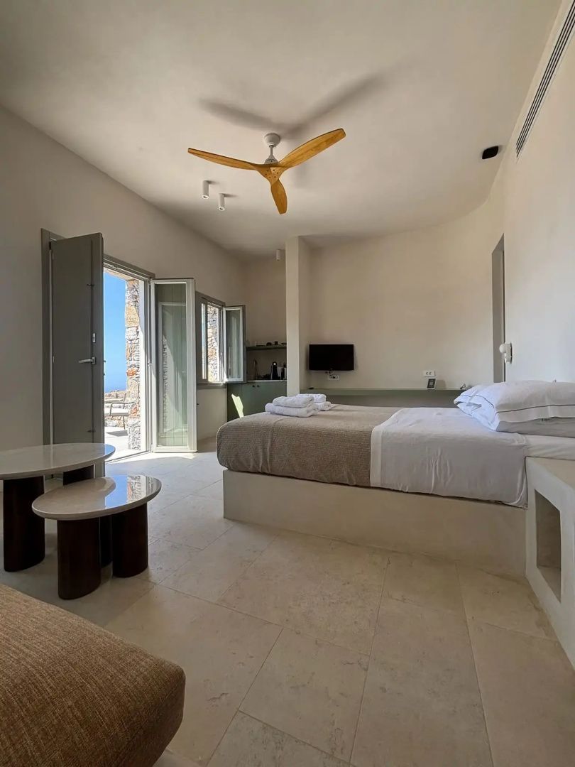 Modernes Schlafzimmer mit Doppelbett, Deckenventilator aus Holz und geöffneter Balkontür.
