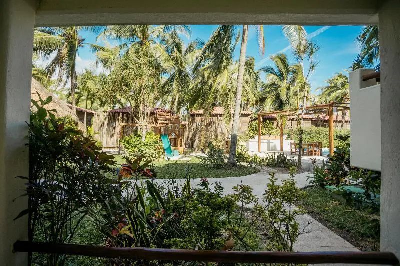 Aussicht von der Terrasse auf die grüne Gartenanlage mit Palmen und Holzbungalows.