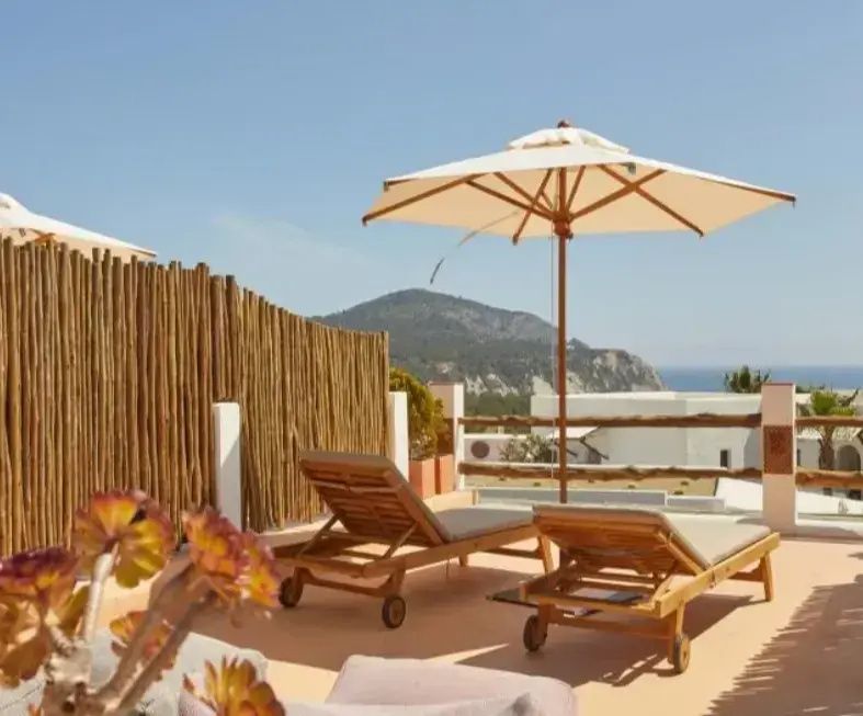 Sonnenterrasse mit zwei Holzliegen, Sonnenschirm und Blick auf Hügel und das Meer.