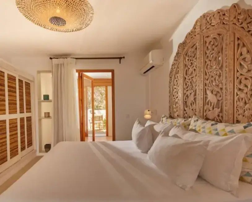 Doppelbett mit verziertem Kopfteil aus Holz und hellen Kissen in einem Hotelzimmer.