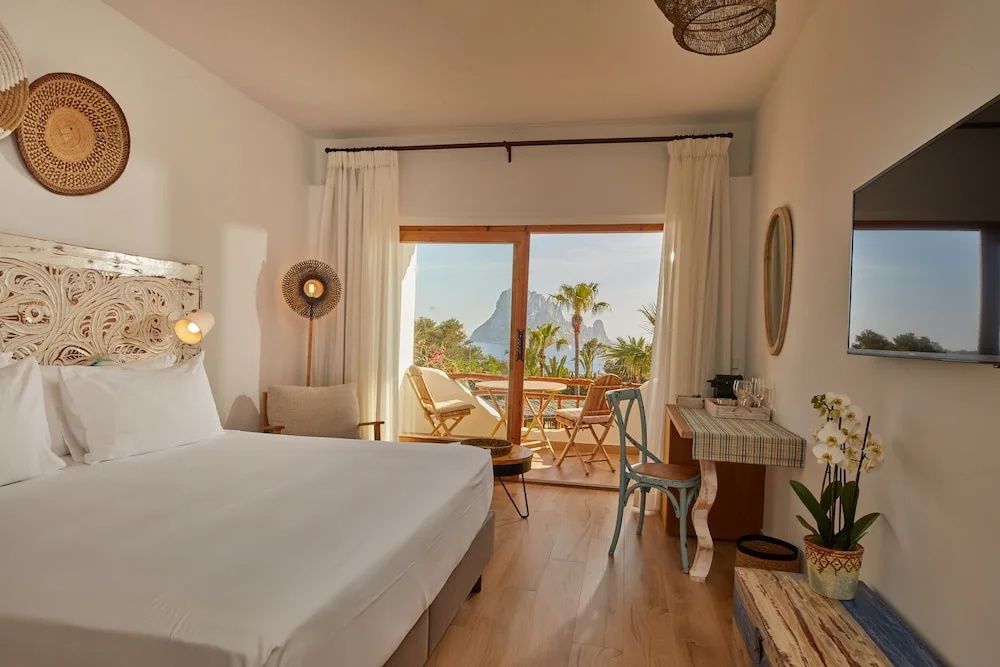 Blick durch die Balkontür auf eine möblierte Terrasse mit Ausblick auf Palmen und das Meer.