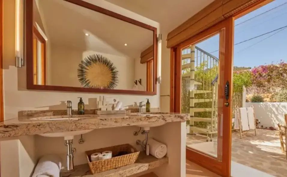 Badezimmer mit zwei Waschbecken, großem Spiegel und Tür zur Terrasse.