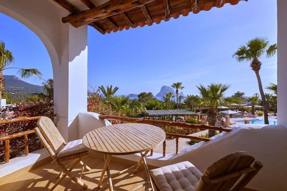 Blick von einem überdachten Balkon mit Holztisch und Stühlen auf den Garten und das Meer.