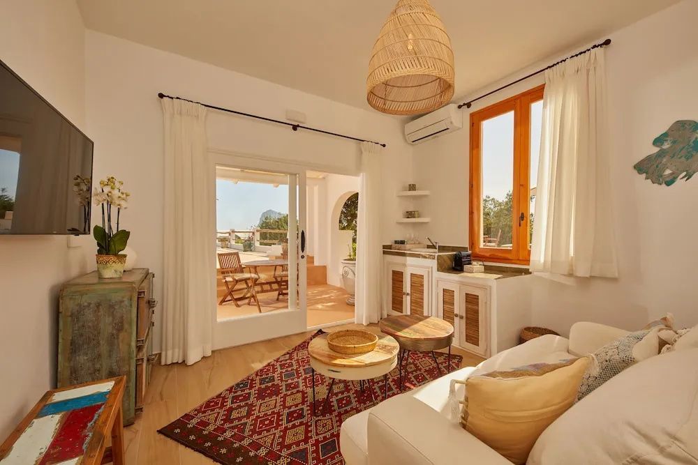 Wohnbereich mit weißem Sofa, rotem Teppich und geöffneter Tür zur Terrasse.