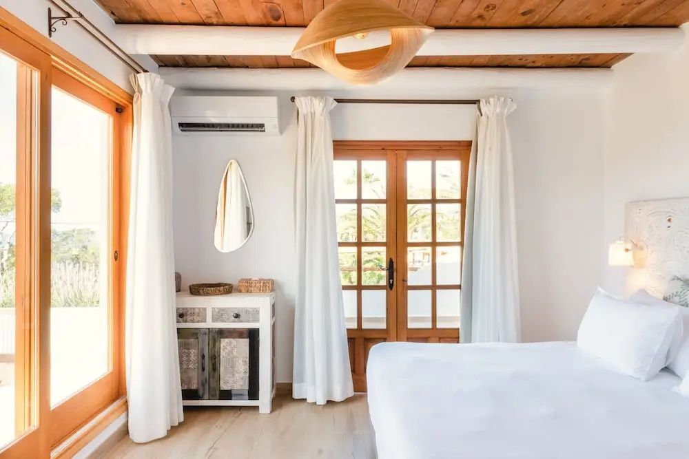 Helles Schlafzimmer mit Holzbalkendecke, einer Kommode und Zugang zum Balkon.