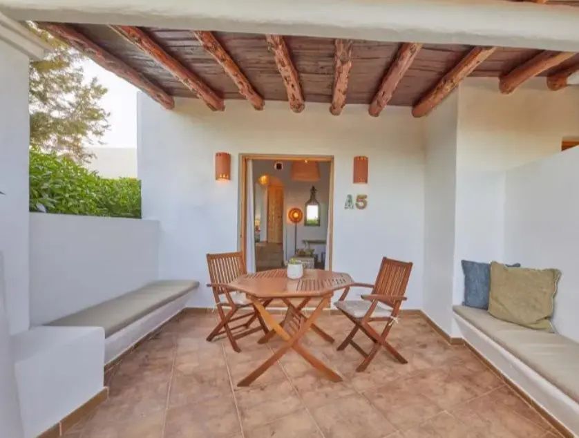 Überdachte Terrasse mit Holztisch, zwei Klappstühlen, Fliesenboden und integrierten Sitzbänken.