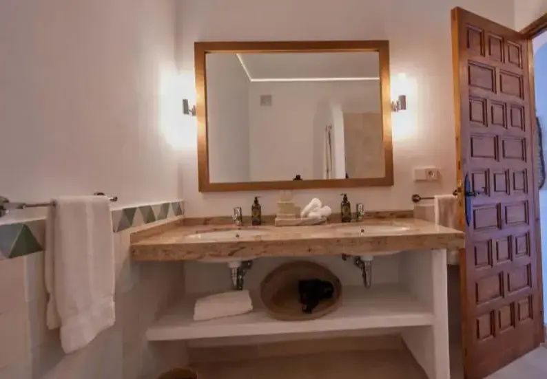 Badezimmer mit Doppelwaschtisch aus Stein, großem Spiegel und warmen Wandleuchten.
