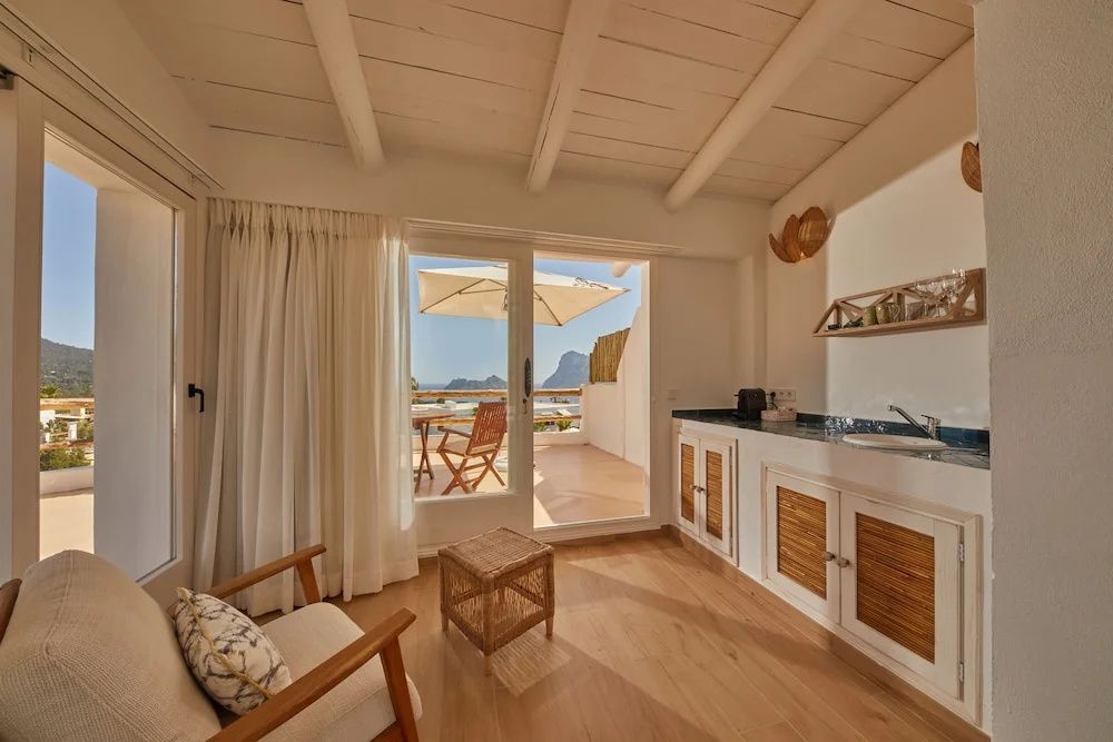 Helles Hotelzimmer mit Holzboden, Kitchenette und Glasflügeltür zur Terrasse mit Meerblick.