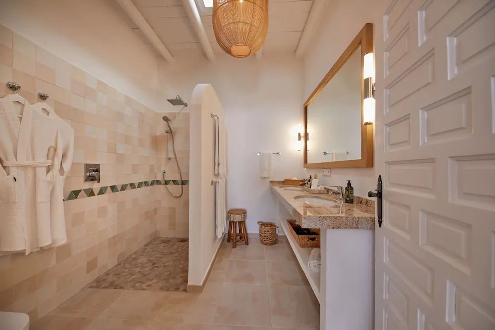 Badezimmer mit ebenerdiger Dusche, langem Waschtisch, großem Spiegel und hellen Fliesen.