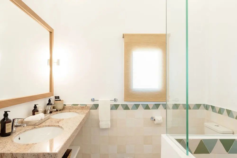 Badezimmer mit doppelter Waschgelegenheit aus Stein, Wandspiegel und einer gläsernen Duschwand.