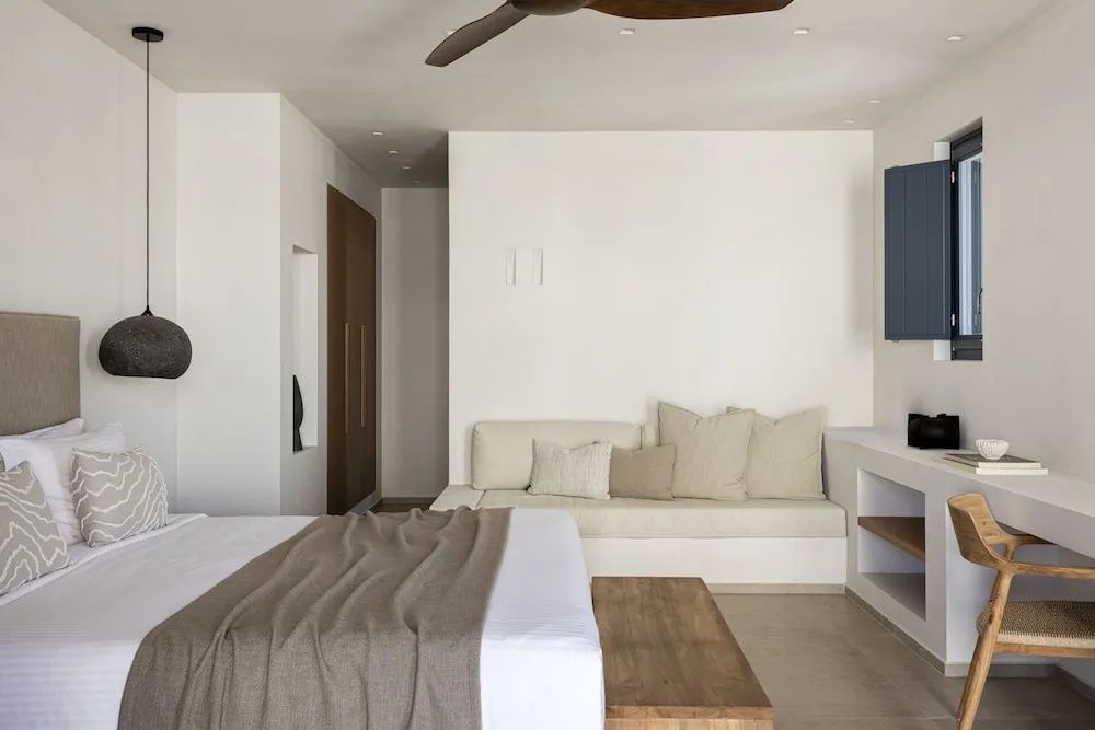 Hell eingerichtetes Schlafzimmer mit Doppelbett, Sitzbank und Deckenventilator.
