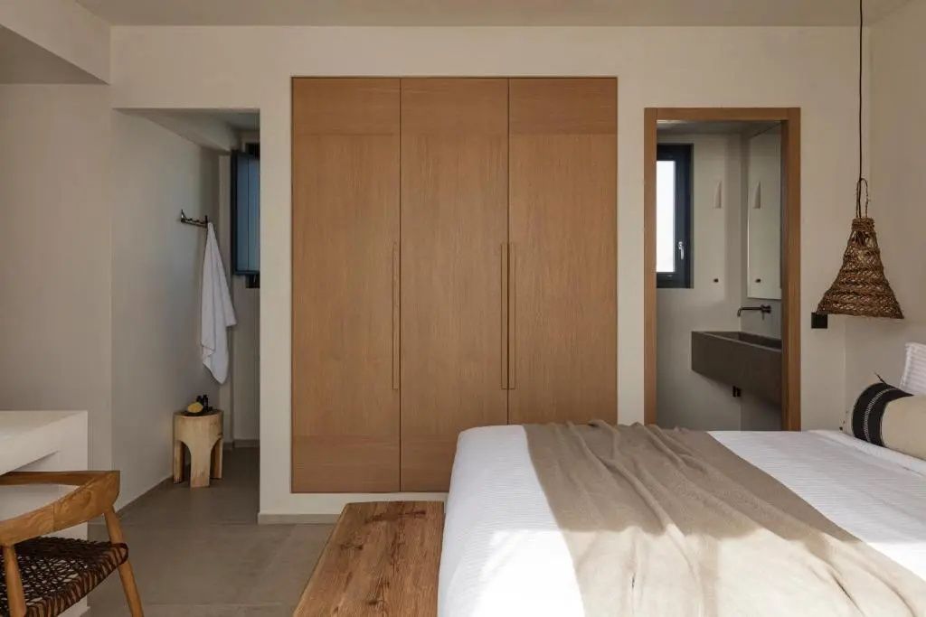 Schlafbereich mit eingebautem Holzschrank, hellem Bett und Durchgang zum Badezimmer.