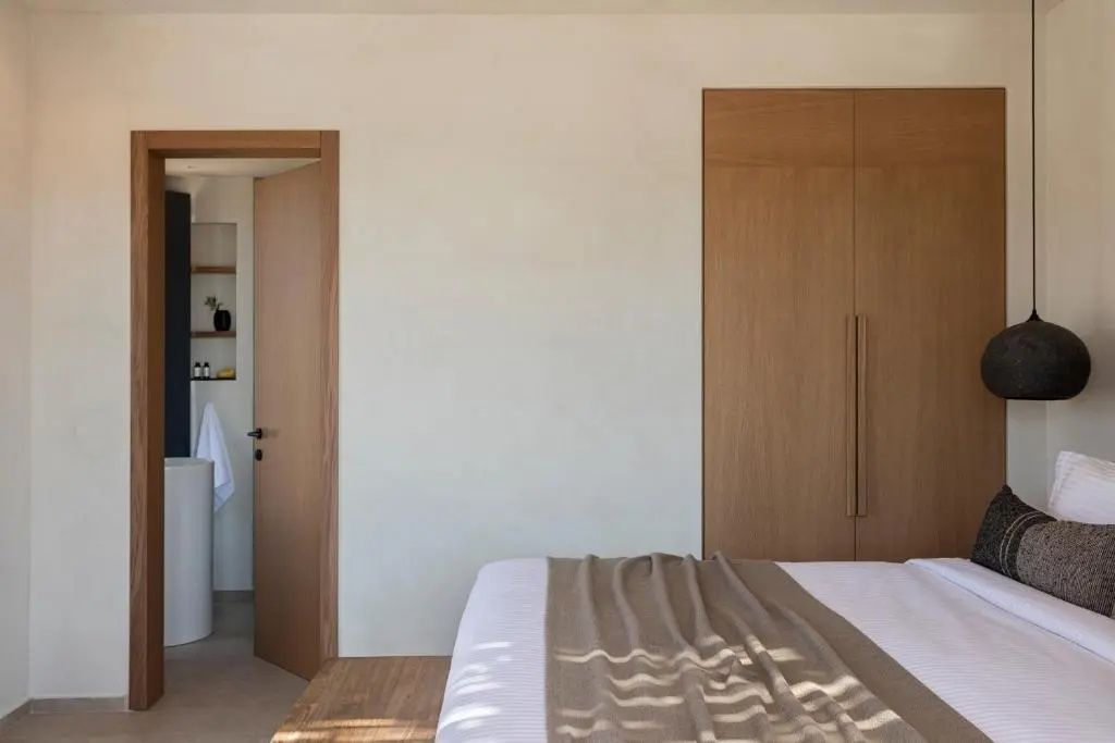 Hell gestaltetes Schlafzimmer mit Holzschrank, Doppelbett und Tür zum Badezimmer.