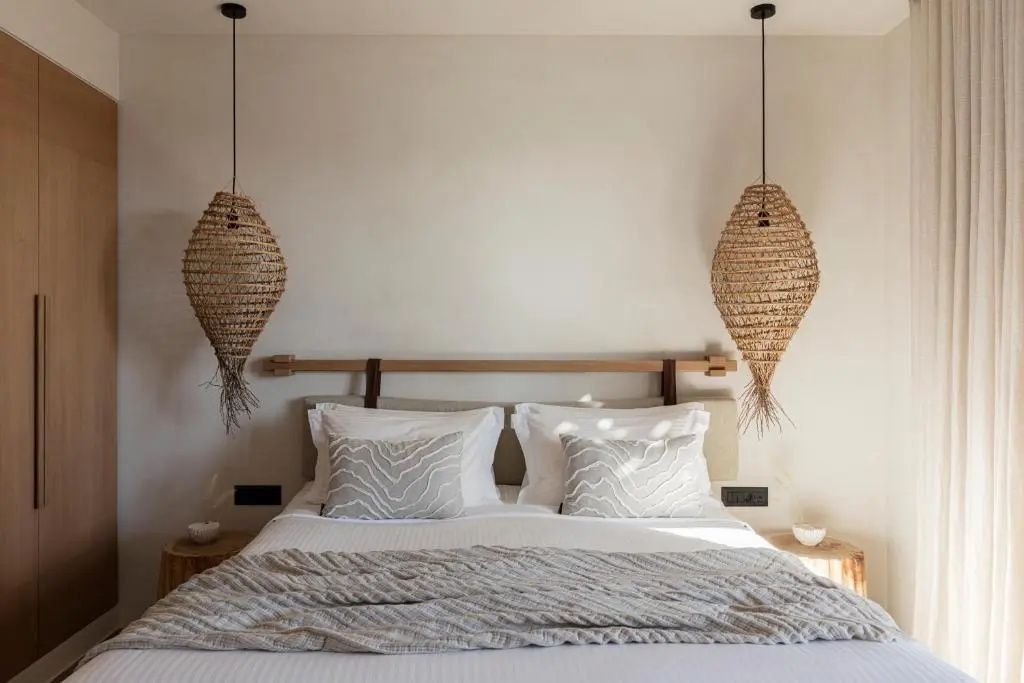 Doppelbett mit hellen Kissen, Tagesdecke und zwei geflochtenen Hängelampen aus Naturmaterial.