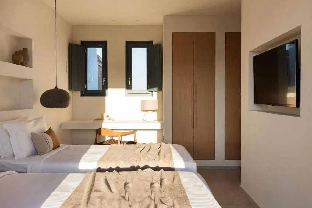Schlafzimmer mit zwei Betten, einem Schreibtisch vor den Fenstern und Holzschrank.