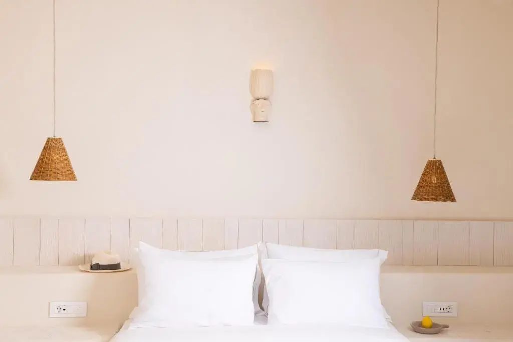 Weißes Doppelbett mit gestärkten Kissen und minimalistischer Wandleuchte im Hotelzimmer.
