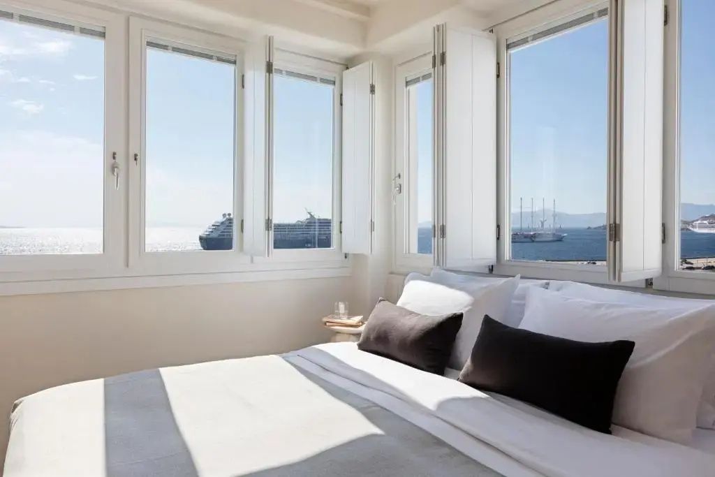 Doppelbett an einer Fensterfront mit Blick auf Schiffe auf dem Meer.