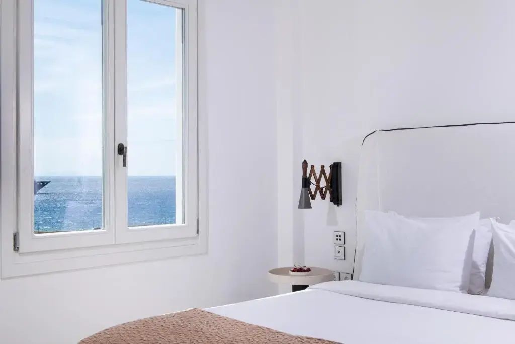 Ausschnitt eines Schlafzimmers mit Fenster zum Meer und einer Wandlampe.